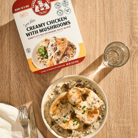 Packaged creamy chicken with mushrooms on a wooden table with a bowl of the dish.