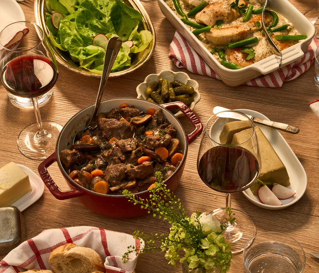 Dining table set with various dishes including a pot of stew, bread, salad, and wine glasses.
